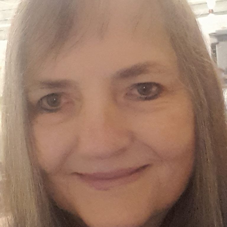 Maria Giesinger Porträt einer lächelnden Frau mit langen, grauen Haaren vor neutralem Hintergrund.